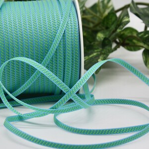 May include: A spool of turquoise and lime green ribbon with a woven pattern. The ribbon is unspooled, with a length of it lying in front of the spool. The ribbon is approximately 0.25 inches wide.