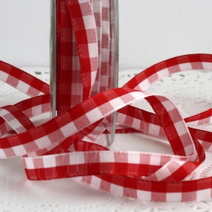 May include: Red and white gingham ribbon, partially spooled in a clear glass container. The ribbon is arranged in loops and curves, showcasing the classic checkered pattern. This decorative ribbon is suitable for crafts and gift wrapping.