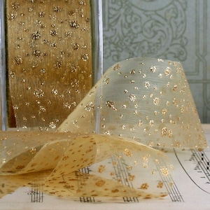 May include: A roll of sheer gold ribbon with a pattern of gold glitter dots. The ribbon is partially unrolled, revealing its delicate texture and sparkle. The ribbon is displayed on a sheet of musical notes.