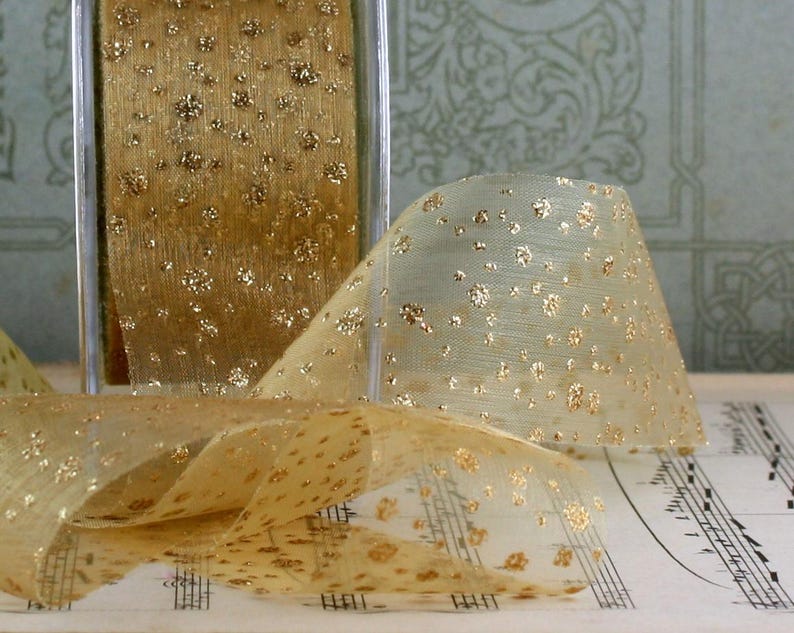 May include: A roll of sheer gold ribbon with a pattern of gold glitter dots. The ribbon is partially unrolled, revealing its delicate texture and sparkle. The ribbon is displayed on a sheet of musical notes.