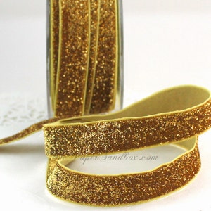 May include: Gold glitter ribbon, displayed in a roll and unrolled. The ribbon has a soft, velvety texture and is covered in sparkling gold glitter. The ribbon is a decorative element, suitable for crafts, gift wrapping, or embellishments.