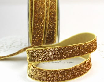 May include: Gold glitter ribbon, displayed in a roll and unrolled. The ribbon has a soft, velvety texture and is covered in sparkling gold glitter. The ribbon is a decorative element, suitable for crafts, gift wrapping, or embellishments.