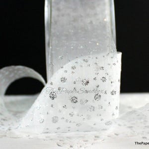 May include: White sheer ribbon with silver glitter detailing. The ribbon is rolled and curled, displaying a delicate, dotted design. The Paper Sandbox logo is visible in the lower right corner.