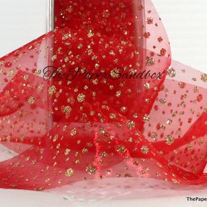 May include: Red sheer ribbon with gold glitter detailing. The ribbon is loosely arranged, showing a portion of the roll. Gold glitter is scattered across the ribbon, creating a festive appearance. The text "The Paper Sandbox" is visible.
