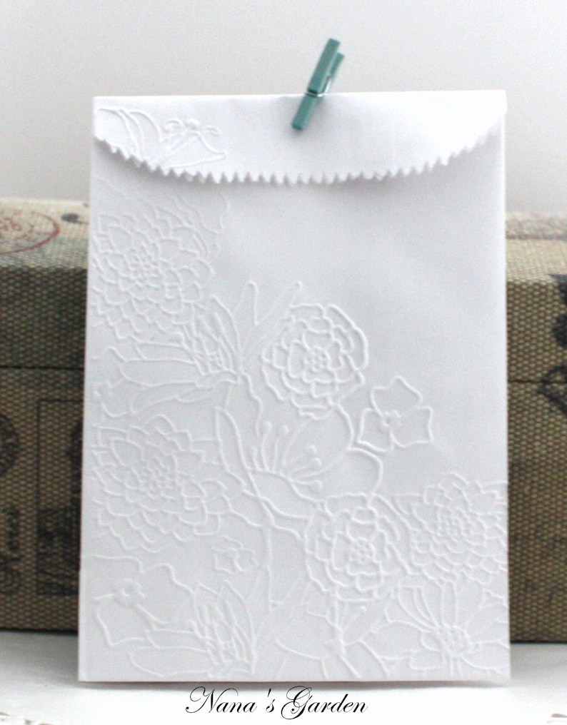 May include: White paper envelope with embossed floral design and a scalloped edge. A small teal clothespin secures the flap. The text "Nana's Garden" is printed at the bottom.