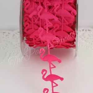 May include: A roll of vibrant pink flamingo ribbon. The ribbon is made of a soft material and features a repeating pattern of flamingo silhouettes. The ribbon is displayed in a clear plastic container.