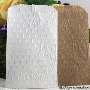 May include: Two paper gift bags, one white and one brown, with embossed honeycomb and bee designs. The white bag has a detailed honeycomb pattern and bee illustrations. The brown bag has a similar design. The PaperSandbox logo is visible.