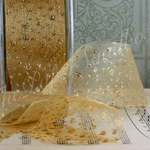 May include: A roll of gold ribbon with a sheer, dotted design. The ribbon is displayed in a clear plastic container, with a section unrolled, showing its texture and pattern. Suitable for crafts and gift wrapping. The ribbon is approximately 2.5 cm wide.
