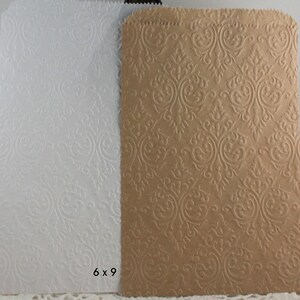 May include: Two paper gift bags, one white and one tan, with an embossed damask pattern. The bags are rectangular, with a folded top edge. The dimensions are 6 x 9 inches.