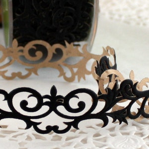 May include: A decorative paper trim with an ornate, scrollwork design. The trim is black on one side and tan on the other, with a repeating pattern of swirling lines and floral elements. The trim is likely used for scrapbooking or other crafts.