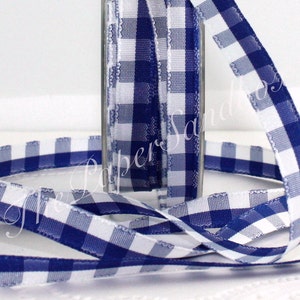 May include: A spool of blue and white gingham ribbon. The ribbon is displayed in a clear glass container and also unraveled, showing the checkered pattern. The ribbon has a scalloped edge.