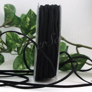 May include: A spool of black suede cord. The cord is tightly wound on a clear plastic spool. The cord is a solid black color and appears to be soft and flexible. Green leafy vines are in the background.