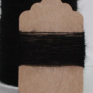 May include: A spool of black twine is wrapped around a brown tag. The twine is tightly wound, and the tag has a decorative shape. The background is a soft white, highlighting the dark twine.