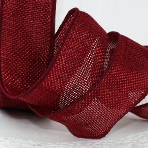 May include: A roll of burgundy ribbon with a woven texture. The ribbon is curled, showing its edges and the weave pattern. The ribbon is a deep red color, suitable for crafts and decorations.