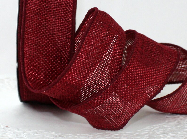 May include: A roll of burgundy ribbon with a woven texture. The ribbon is curled, showing its edges and the weave pattern. The ribbon is a deep red color, suitable for crafts and decorations.