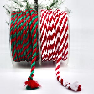 May include: Two spools of decorative rope. One spool features red and green twisted rope, and the other has red and white twisted rope. The rope is wound on clear plastic spools, perfect for holiday crafts and gift wrapping.