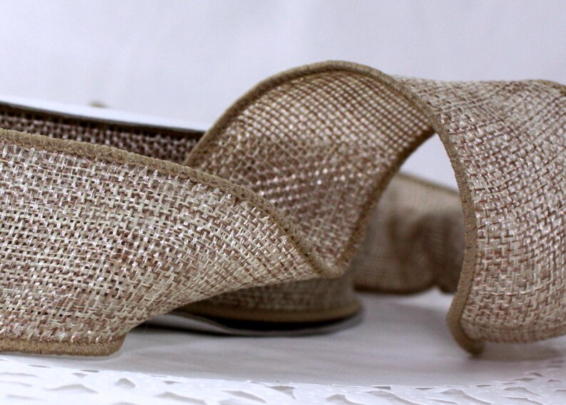 May include: Close-up of a roll of natural-colored burlap ribbon. The ribbon has a woven texture with a brown edge. The ribbon is curled, showing the front and back of the material. This ribbon is suitable for crafts and decorations.
