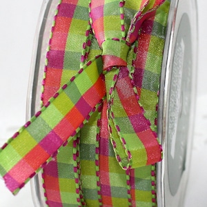 May include: A spool of decorative ribbon with a vibrant plaid pattern in shades of green, pink, and orange. The ribbon is tied into a bow, and the edges are finished with a contrasting pink stitching. The ribbon is on a clear plastic spool.
