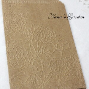 May include: A small, brown paper bag with a floral embossed design. The bag has a scalloped top edge and the text "Nana's Garden" in a script font.