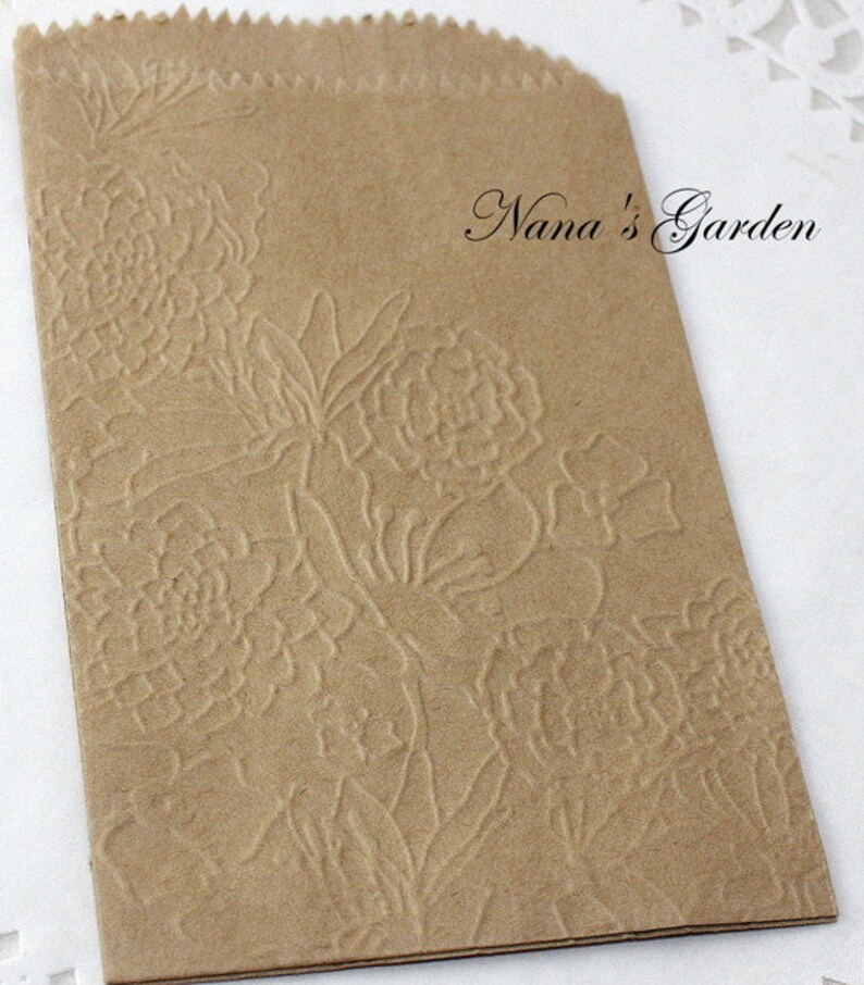 May include: A small, brown paper bag with a floral embossed design. The bag has a scalloped top edge and the text "Nana's Garden" in a script font.