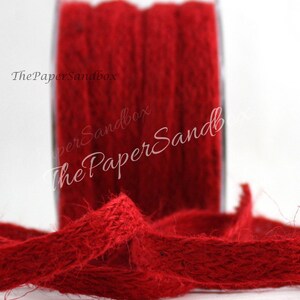 Op de afbeelding: Een spoel levendig rood jute lint. Het lint is strak op een transparante spoel gewikkeld, met een lengte van het lint afgerold op de voorgrond. De tekst "ThePaperSandbox" is zichtbaar op de afbeelding. Dit lint is geschikt voor knutselen en decoraties.