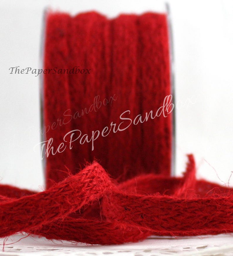 Op de afbeelding: Een spoel levendig rood jute lint. Het lint is strak op een transparante spoel gewikkeld, met een lengte van het lint afgerold op de voorgrond. De tekst "ThePaperSandbox" is zichtbaar op de afbeelding. Dit lint is geschikt voor knutselen en decoraties.