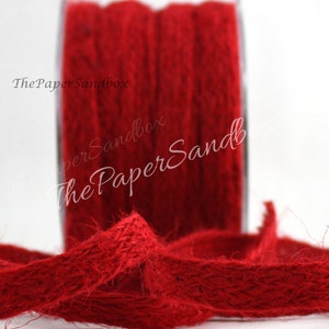 May include: A spool of red burlap ribbon. The ribbon is a deep, rich red color and appears to be made of natural fibers. The spool is partially visible, with the ribbon unwound in the foreground. The text "The PaperSandbox" is visible.