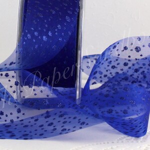 May include: A roll of sheer royal blue ribbon with a delicate floral pattern. The ribbon is partially unrolled, revealing its texture and design. The ribbon is ideal for gift wrapping, crafting, or decorative purposes.