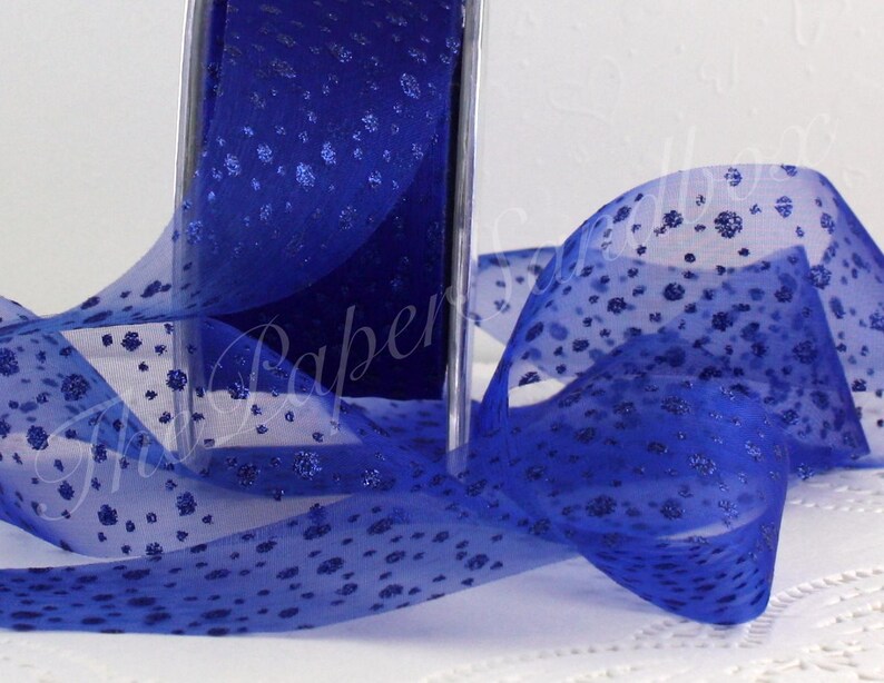 May include: A roll of sheer royal blue ribbon with a delicate floral pattern. The ribbon is partially unrolled, revealing its texture and design. The ribbon is ideal for gift wrapping, crafting, or decorative purposes.