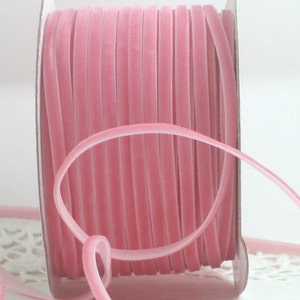 May include: A spool of soft, pink velvet ribbon. The ribbon is tightly wound on a cardboard spool, with a length of ribbon looped in the foreground. The ribbon has a smooth, velvety texture and a delicate, pastel color.