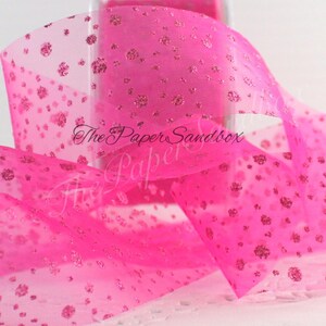 May include: Bright pink sheer ribbon with glitter accents. The ribbon has a dotted pattern of glitter and the text "The Paper Sandbox" is visible. This ribbon is suitable for crafts, gift wrapping, and decorations.