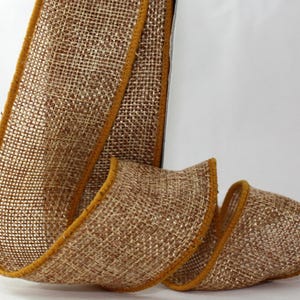 May include: A roll of burlap ribbon with a woven texture. The ribbon is a natural brown color with a gold trim along the edges. The ribbon is curled and displayed against a white background.