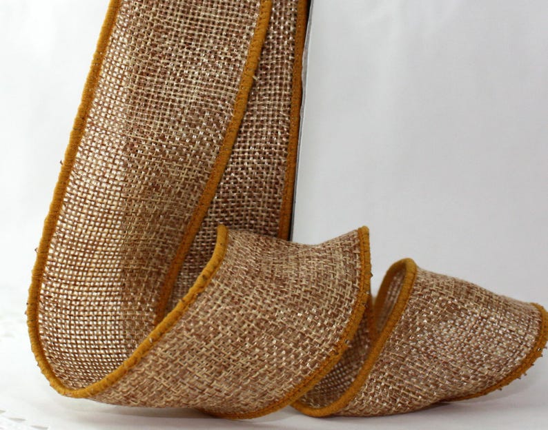 May include: A roll of burlap ribbon with a woven texture. The ribbon is a natural brown color with a gold trim along the edges. The ribbon is curled and displayed against a white background.