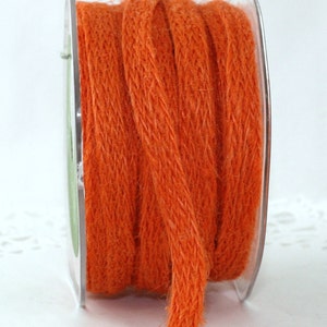 Op de afbeelding: Een spoel oranje jute touw. Het touw is strak opgerold op een transparante plastic spoel. Het touw heeft een getextureerde, geweven uitstraling en een levendige, effen oranje kleur.