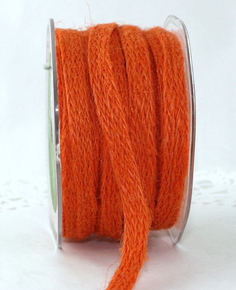 Op de afbeelding: Een spoel oranje jute touw. Het touw is strak opgerold op een transparante plastic spoel. Het touw heeft een getextureerde, geweven uitstraling en een levendige, effen oranje kleur.