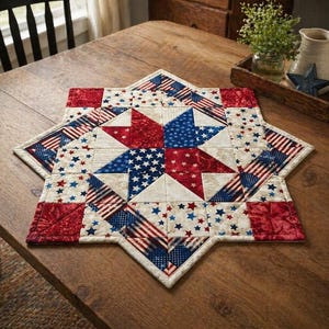 May include: A star-shaped quilted table topper in red, white, and blue. The design features stars, stripes, and patriotic patterns. The table topper is placed on a wooden table.