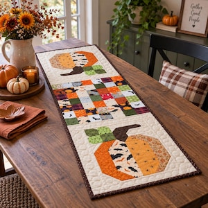May include: A rectangular quilted table runner featuring two large pumpkin motifs at the ends and a central section of multicolored patchwork squares. The fabric patterns include orange, green, and black prints with bats and autumn-themed designs.