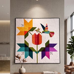 May include: A colorful quilt featuring a floral design with hummingbirds. The quilt showcases a central tulip and star-shaped flowers in shades of orange, yellow, teal, and purple. Two hummingbirds are depicted, one in flight. The quilt is framed in black.