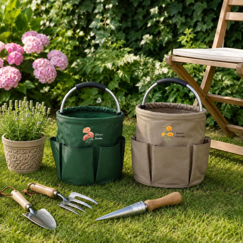 Puede incluir: Dos bolsas de jard&iacute;n cil&iacute;ndricas con asas plateadas y bolsillos exteriores. La bolsa verde oscuro tiene un gr&aacute;fico de flor naranja y el texto "Selina's Garden", mientras que la beige muestra una flor amarilla y "Mom's Garden".