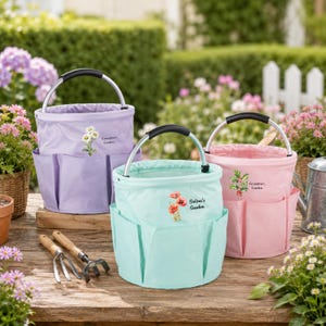 Puede incluir: Tres bolsas de jard&iacute;n redondas de tela en lavanda, verde menta y rosa claro, cada una con asa de metal y bolsillos exteriores. La bolsa lavanda tiene un gr&aacute;fico de margaritas, la verde menta tiene amapolas y la rosa tiene una rama floral.