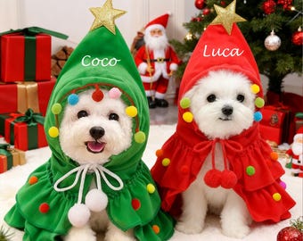 May include: Two small white dogs wearing Christmas tree costumes. One is green with the name "Coco" on the hood, and the other is red with the name "Luca". Both costumes have gold star toppers and colorful pom-poms.