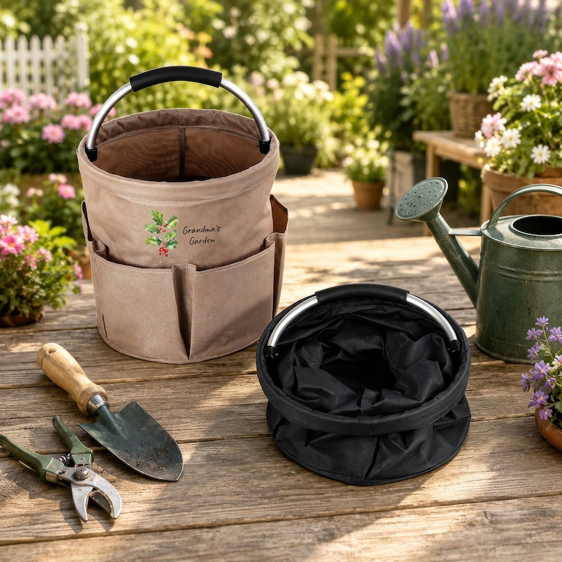 Puede incluir: Una bolsa de jard&iacute;n de lona color canela con m&uacute;ltiples bolsillos exteriores y un asa plateada, con un gr&aacute;fico de acebo y el texto Grandma's Garden. Al lado hay un cubo de tela negro plegado, una paleta de mano y unas tijeras de podar.