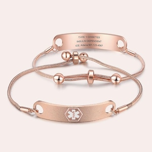 May include: Two rose gold medical alert bracelets. The top bracelet has the text "TYPE 1 DIABETES INSULIN DEPENDENT" and contact information. The bottom bracelet has a medical symbol. Both bracelets have a delicate chain design.
