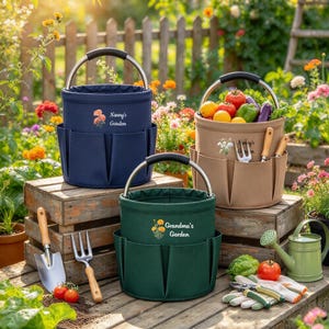 Puede incluir: Tres bolsas cil&iacute;ndricas para herramientas de jard&iacute;n en azul marino, verde oscuro y beige, cada una con asa de metal y bolsillos exteriores. Las bolsas incluyen gr&aacute;ficos florales y el texto Nanny's Garden y Grandma's Garden.