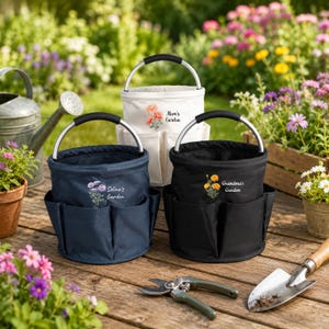 Puede incluir: Tres bolsas cil&iacute;ndricas para herramientas de jard&iacute;n en azul marino, blanco y negro, cada una con asa de metal plateado, bolsillos exteriores y un gr&aacute;fico floral con el texto Mom's Garden, Selina's Garden o Grandma's Garden.
