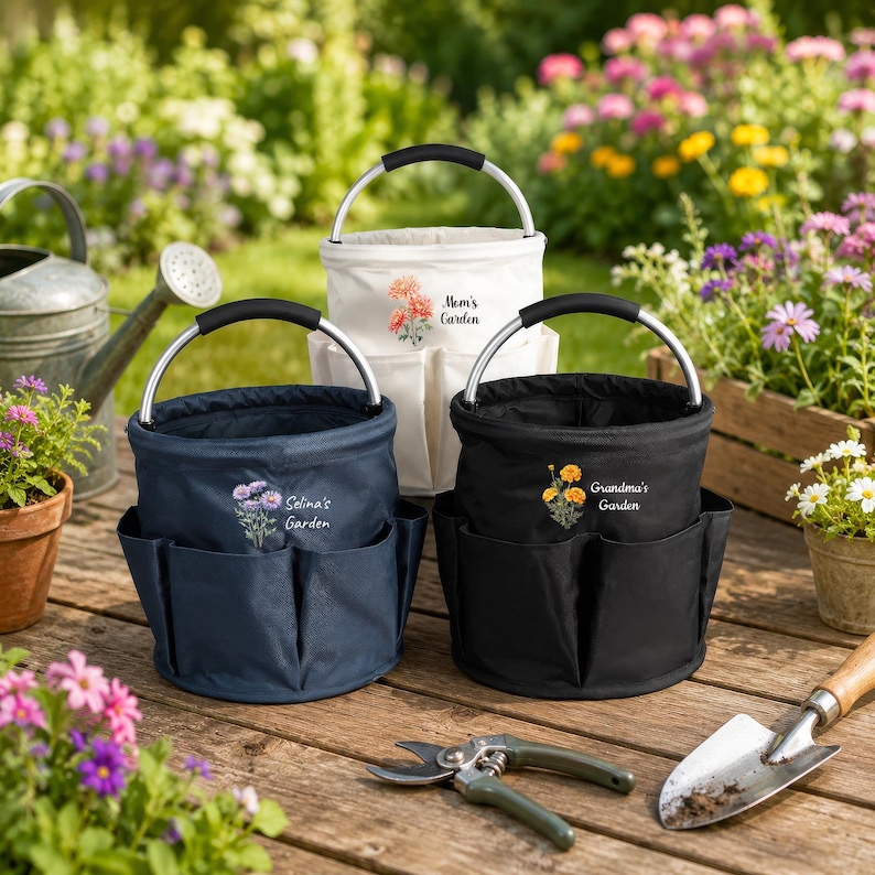 Puede incluir: Tres bolsas cil&iacute;ndricas para herramientas de jard&iacute;n en azul marino, blanco y negro, cada una con asa de metal plateado, bolsillos exteriores y un gr&aacute;fico floral con el texto Mom's Garden, Selina's Garden o Grandma's Garden.