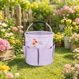 Puede incluir: Una bolsa de jard&iacute;n de tela color morado claro con asa de metal plateado y varios bolsillos exteriores. El frente presenta una ilustraci&oacute;n de amapolas rojas y el texto Selina's Garden en una fuente cursiva oscura.