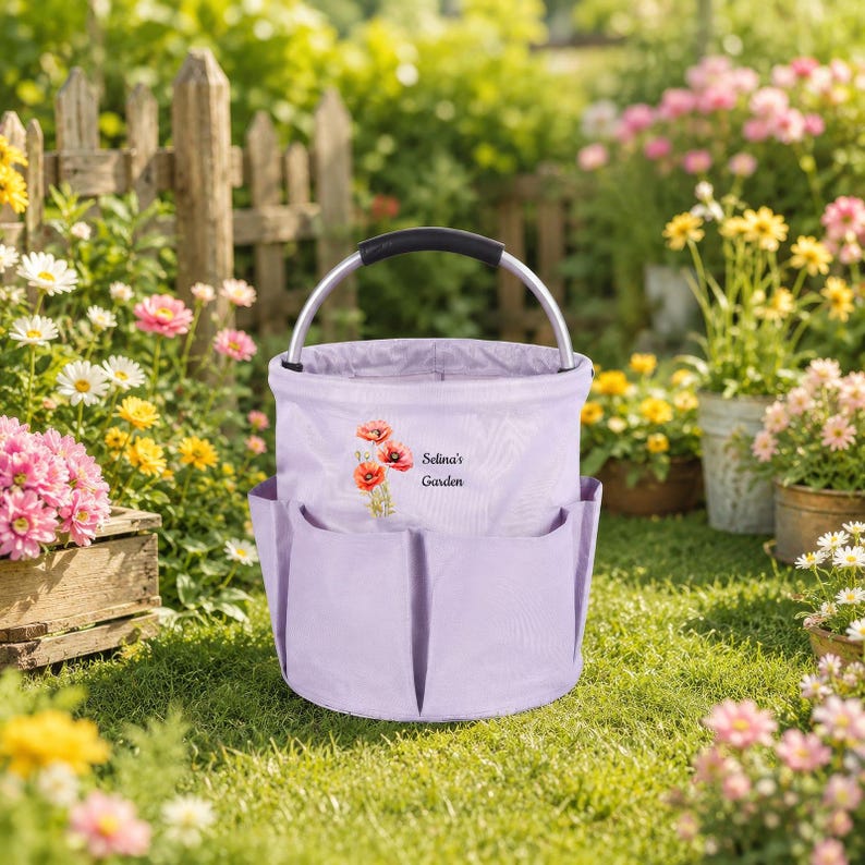 Puede incluir: Una bolsa de jard&iacute;n de tela color morado claro con asa de metal plateado y varios bolsillos exteriores. El frente presenta una ilustraci&oacute;n de amapolas rojas y el texto Selina's Garden en una fuente cursiva oscura.