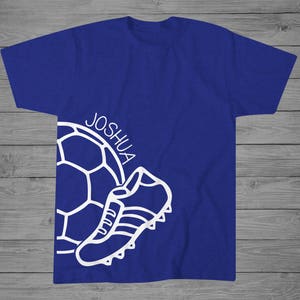May include: A royal blue t-shirt with a white outline of a soccer ball and a soccer cleat. The name "Joshua" is written on the shirt.