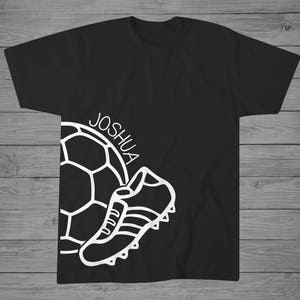 May include: Black t-shirt with a white outline of a soccer ball and a soccer cleat. The text "JOSHUA" is written on the shirt.
